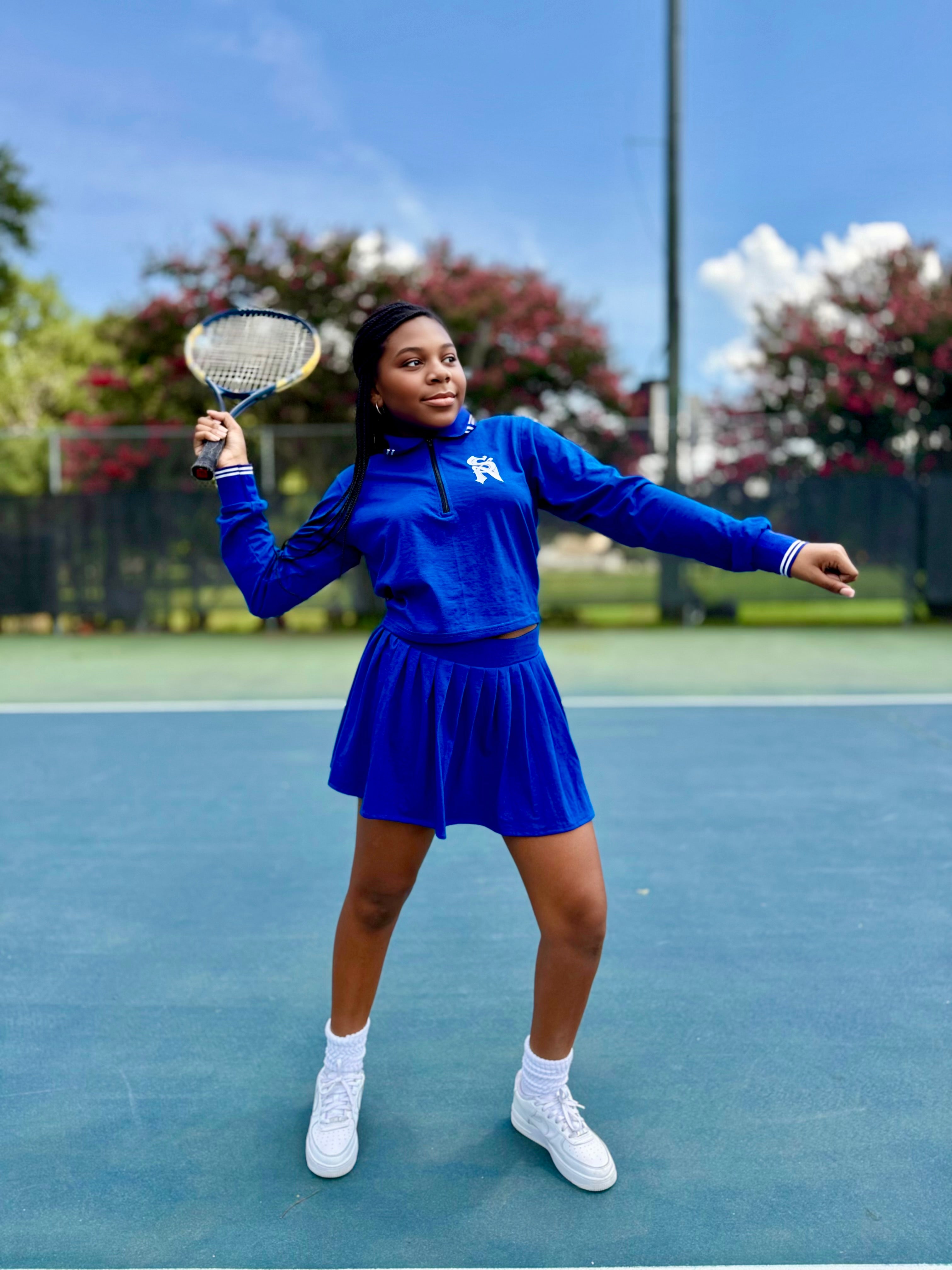 Small Girl in a blue STACK NATION LLC tennis outfit holding a racket on a tennis court